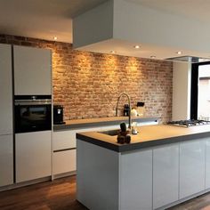 a kitchen with white cabinets and an island in front of a brick wall that looks like it has been built into the side of a house