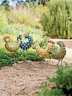 three metal roosters sitting on top of a patch of green grass next to bushes