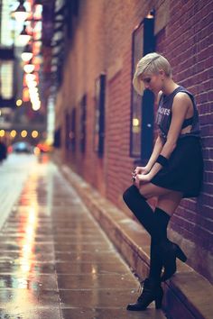 a woman leaning against a brick wall with her legs crossed and looking at her phone