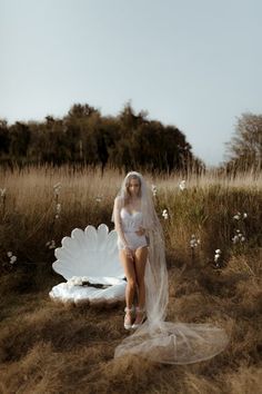 a woman in a white wedding dress sitting on a shell shaped object with her legs crossed