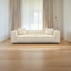 a white couch sitting in front of a window next to a lamp and wooden floor