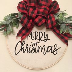 a merry christmas sign with red and black plaid bow hanging from the front of a hoop