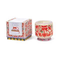 a candle that is next to a box on a white surface with an orange and red design