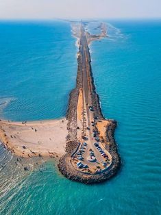 an aerial view of the ocean with cars parked on it's sides and a long pier in the middle