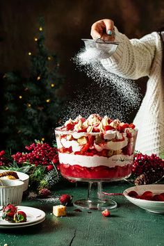 a woman sprinkling icing onto a layered cake with strawberries on top