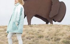 a woman standing in front of a large elephant statue on top of a hill next to a grass covered field