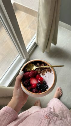 a person is holding a bowl of food with berries and yogurt in it