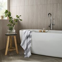 a white bath tub sitting next to a wooden stool with a potted plant on it