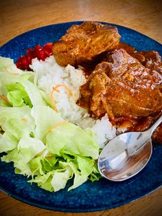 a blue plate topped with meat and rice next to a salad on top of a wooden table