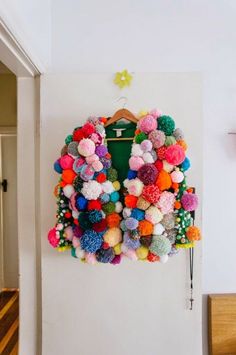 a colorful jacket hanging on a wall with pom - poms all over it