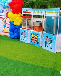 an ice cream kiosk with balloons on the grass in front of a carnival sign