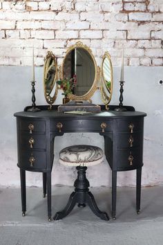 an antique vanity with mirror and stool in front of a brick wall, next to a candle holder