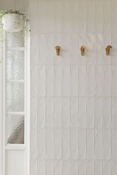 three brass hooks are on the wall next to a white tiled bathroom with a window