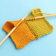 two knitting needles are next to an orange and green knitted bag on a blue surface