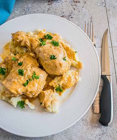 a white plate topped with chicken covered in gravy next to a knife and fork