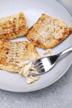 two pieces of chicken on a plate with a fork and knife next to it,