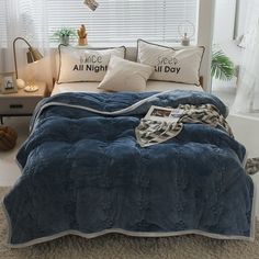 a bed with blue comforter and pillows on it in front of a large window