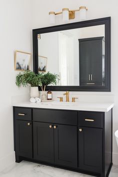 a bathroom with black cabinets and white counter tops, gold accents on the mirror over the sink