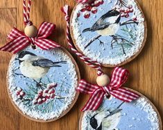 three christmas ornaments with birds on them hanging from red and white ribbons, sitting on a wooden surface