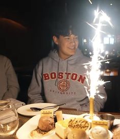 two people sitting at a table with food and drinks in front of them, one holding a sparkler