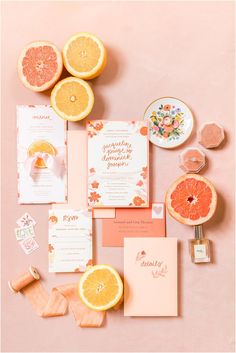 an assortment of wedding stationery with oranges and other items on a pink background