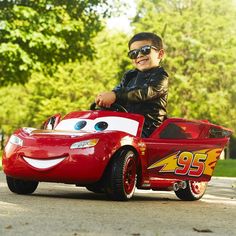 a young boy riding on the back of a red toy car with a smiling face