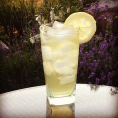 a glass filled with lemonade sitting on top of a table next to purple flowers