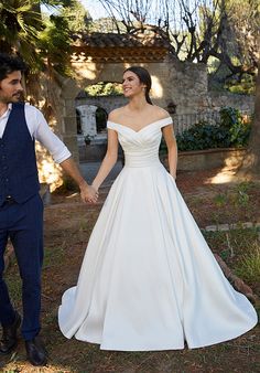 a bride and groom hold hands as they walk through the grass