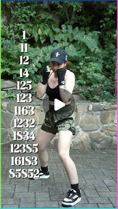 a woman in black shirt and green shorts standing on brick floor next to trees with numbers behind her