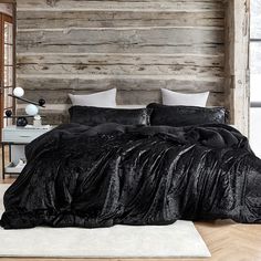 a bed with black sheets and pillows in a rustic style bedroom, next to a wooden wall