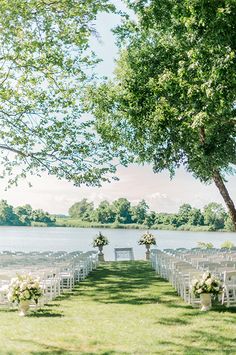 an outdoor ceremony setup with white chairs and flowers on the grass by the water is ready for guests to sit down