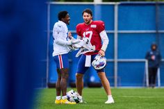 two football players talking to each other on the field in front of a blue wall