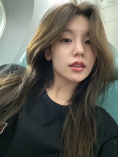 a woman with long hair sitting on an airplane looking at the camera while wearing a black t - shirt