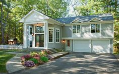 a large house in the middle of a wooded area with lots of trees and flowers