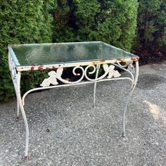 a glass table sitting on top of gravel next to some bushes and trees in the background