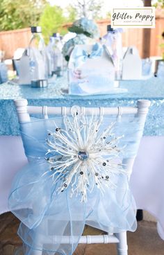 a blue table with white chair covers and flowers on the back of it is set up for a baby's first birthday party