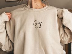 This soft cozy Golf Mom sweatshirt is the perfect gift for yourself or any golf sports mama you know! It is a great minimal sweatshirt to wear during your everyday life or to your kid's golf practice or tournament. :) It also makes the perfect thoughtful gift for a mom you love.  ⋒ ORDER INFORMATION ⋒ Ideal for any situation, a unisex heavy blend crewneck sweatshirt is pure comfort. These garments are made from polyester and cotton. This combination helps designs come out looking fresh and beautiful. The collar is ribbed knit, so it retains its shape even after washing. There are no itchy side seams on these sweaters. .: 50% Cotton 50% Polyester .: Medium-heavy fabric (8.0 oz/yd² (271.25 g/m .: Loose fit .: Sewn in label .: Runs true to size Please note that this listing is for one sweatsh Minimal Sweatshirt, Outfit Minimal, Golf Mom, Sport Mom, Mom Outfit, Kids Golf, Golf Practice, Mom Sweater, Golf Tournament