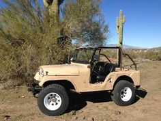 an old jeep is parked in the desert near a cactus tree and a large saguado