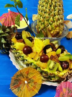 pineapples, grapes, and other fruits are arranged on a platter with umbrellas