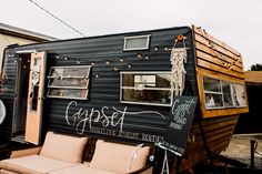 a tiny black trailer parked in front of a house with two couches next to it