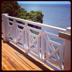 a balcony with white railings overlooking the water and trees in the distance on a sunny day