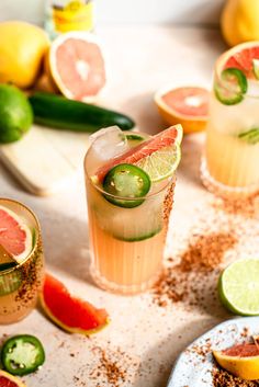 two glasses filled with drinks sitting on top of a table next to slices of watermelon and cucumber