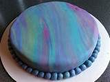 a round cake with blue and purple icing on a white plate sitting on a table