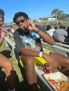 two young men sitting next to each other at a baseball game, one eating food