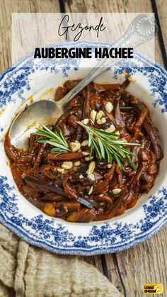 a bowl filled with meat and vegetables on top of a wooden table next to a spoon