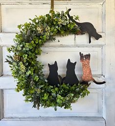 a wreath with three cats hanging from it's sides and some leaves on the front door