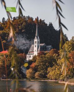 an old church sits on top of a hill next to a body of water with trees around it