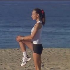 a woman sitting on top of a sandy beach next to the ocean