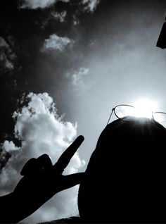 the silhouette of a person holding their hand up to the sky with clouds in the background