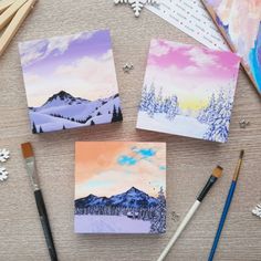 four paintings are sitting on a table with paintbrushes and snowflakes around them